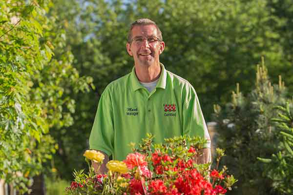 An employee pushing a cart of roses and other plants at a garden center.